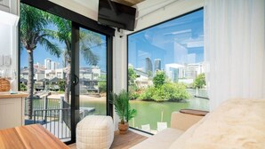 A balcony with a city view, a wooden table, a cushioned bench, and a potted plant. - Tiny Home in the heart of Broadbeach-River Views! (Broadbeach Waters)