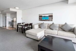 Ein modernes Wohnzimmer mit Sofa, Hocker, Couchtisch und einem Essbereich mit Stühlen und Tisch.