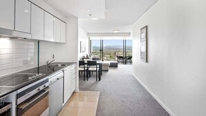 A modern kitchen with a view to the outdoors, a dining area with a table and chairs, and a large window. - City & Hinterland Views – 1BR Retreat in Sierra Broadbeach (Gold Coast)