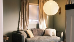 A living room with a sofa, a coffee table, and a hanging light fixture. - The Vinyl House: Olde Town - King Bed - EV Charger - Epic Views - Designer Home (Arvada)