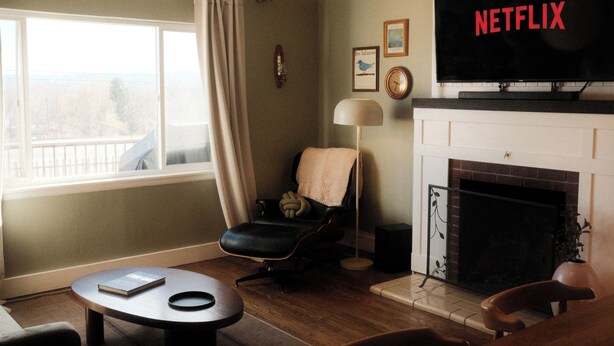 A living room with a fireplace, a television displaying 'NETFLIX,' a window with curtains, and a bookshelf. - The Vinyl House: Olde Town - King Bed - EV Charger - Epic Views - Designer Home (Arvada)