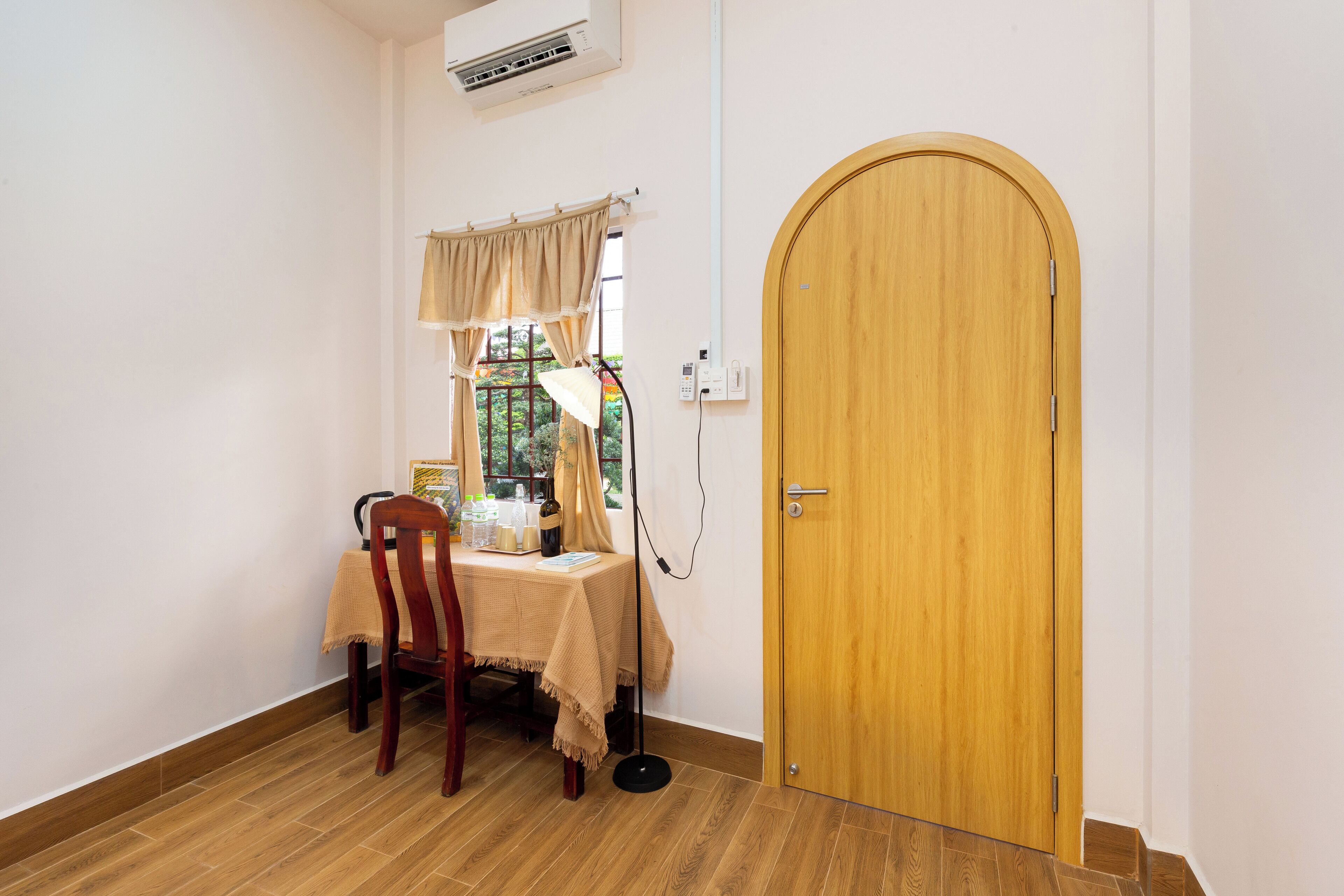 Une pièce avec une porte en bois, une table recouverte d’une nappe, une chaise, une lampe et une fenêtre avec des rideaux.