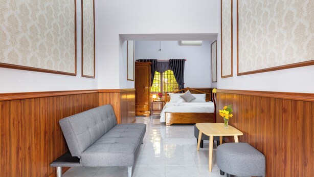 A hotel room with a sofa, a bed, a small table with a vase of flowers, and a wooden wall paneling. - SaDec Farmstay (Sa Dec)