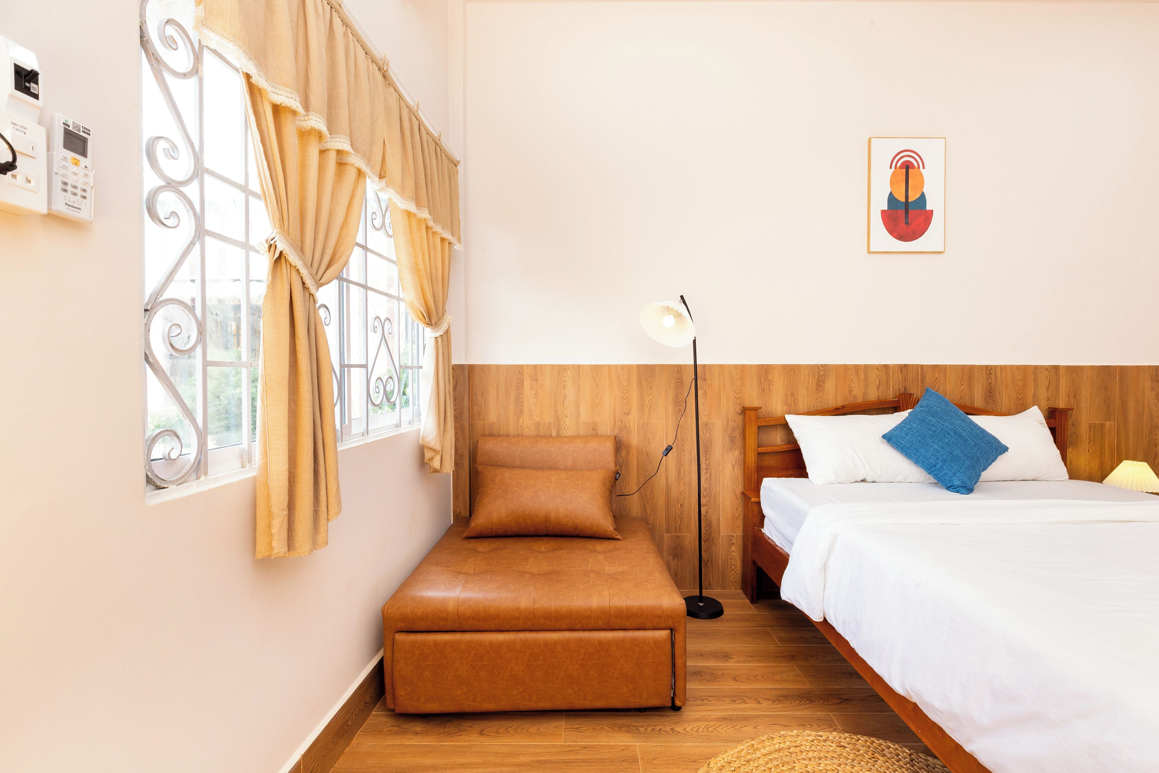 Un dormitorio con cama, un banco, una lámpara de pie y una ventana con cortinas.