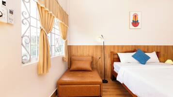 Un dormitorio con cama, un banco, una lámpara de pie y una ventana con cortinas.