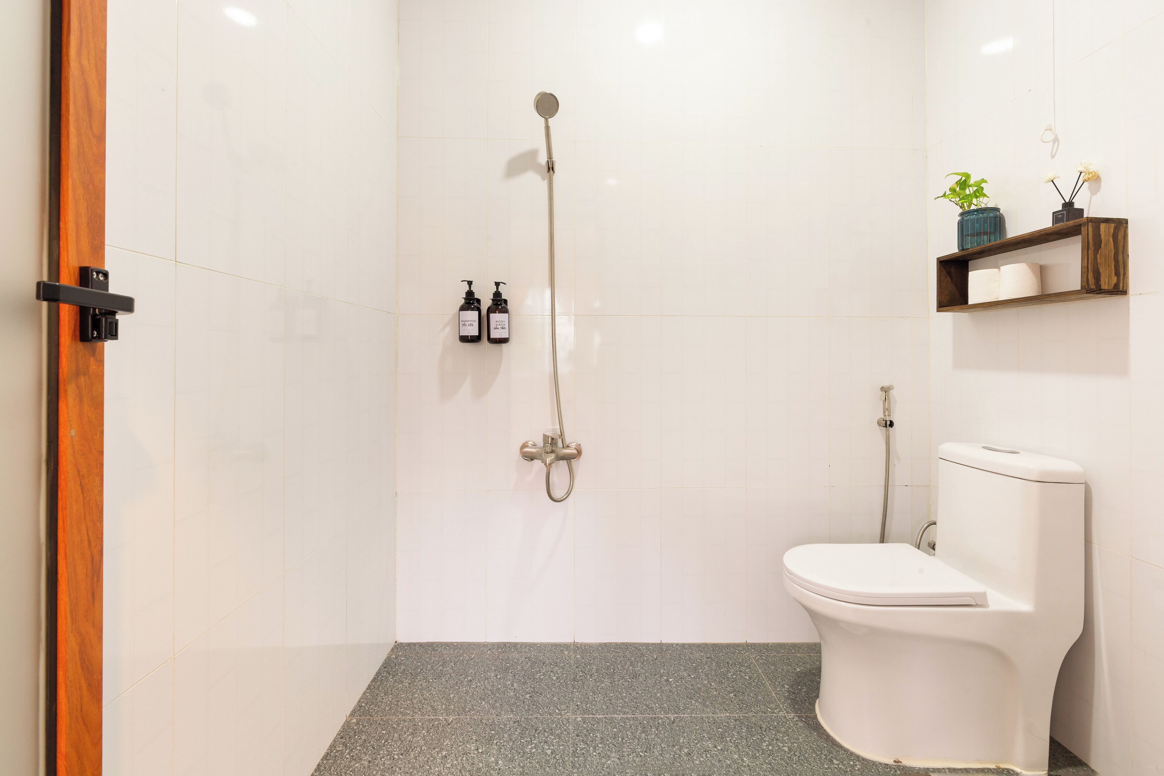 Een moderne badkamer met een douche, toilet en twee flessen toiletartikelen aan de muur.