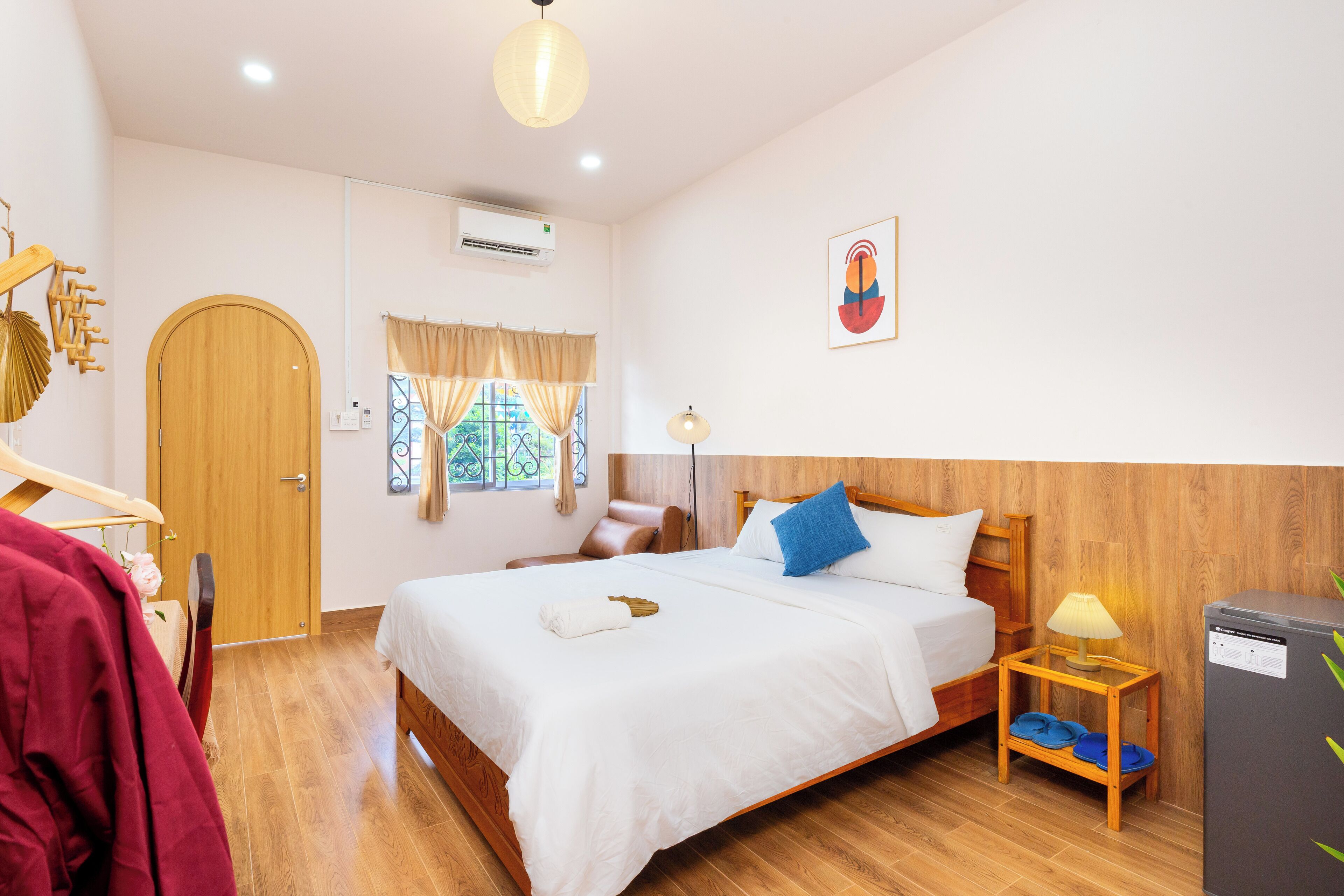 Una habitación de hotel con una cama de madera, una mesita con una lámpara, un armario y una ventana con cortinas.