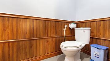 Une salle de bain avec des toilettes blanches, un lambris en bois et une poubelle bleue.