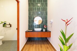 A bathroom with a wooden vanity, a round mirror, a white sink, and a green tiled wall. - SaDec Farmstay (Sa Dec)