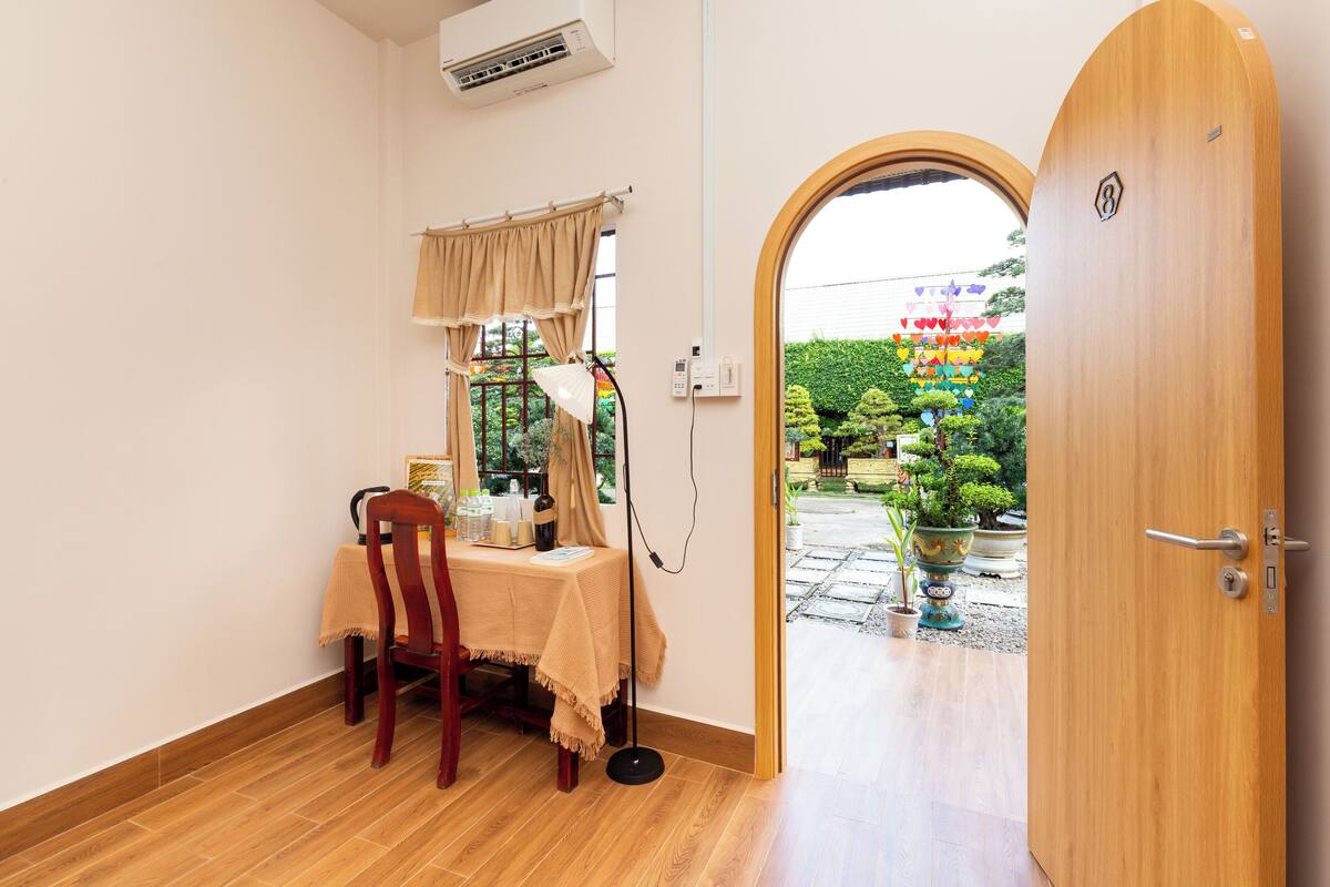 Une pièce avec une porte en bois, une table recouverte d’une nappe beige, une chaise et une fenêtre avec des rideaux.