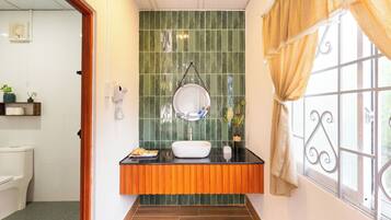 Un baño con un lavamanos blanco, salpicadero de azulejos verdes y una ventana con cortina.