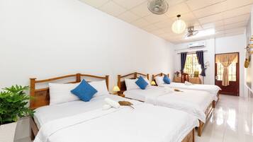 A hotel room with three wooden beds, white bedding, and a potted plant.