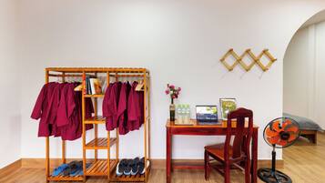 Una habitación con un zapatero de madera, un escritorio con una computadora portátil, un ventilador y un estante fijado a la pared.