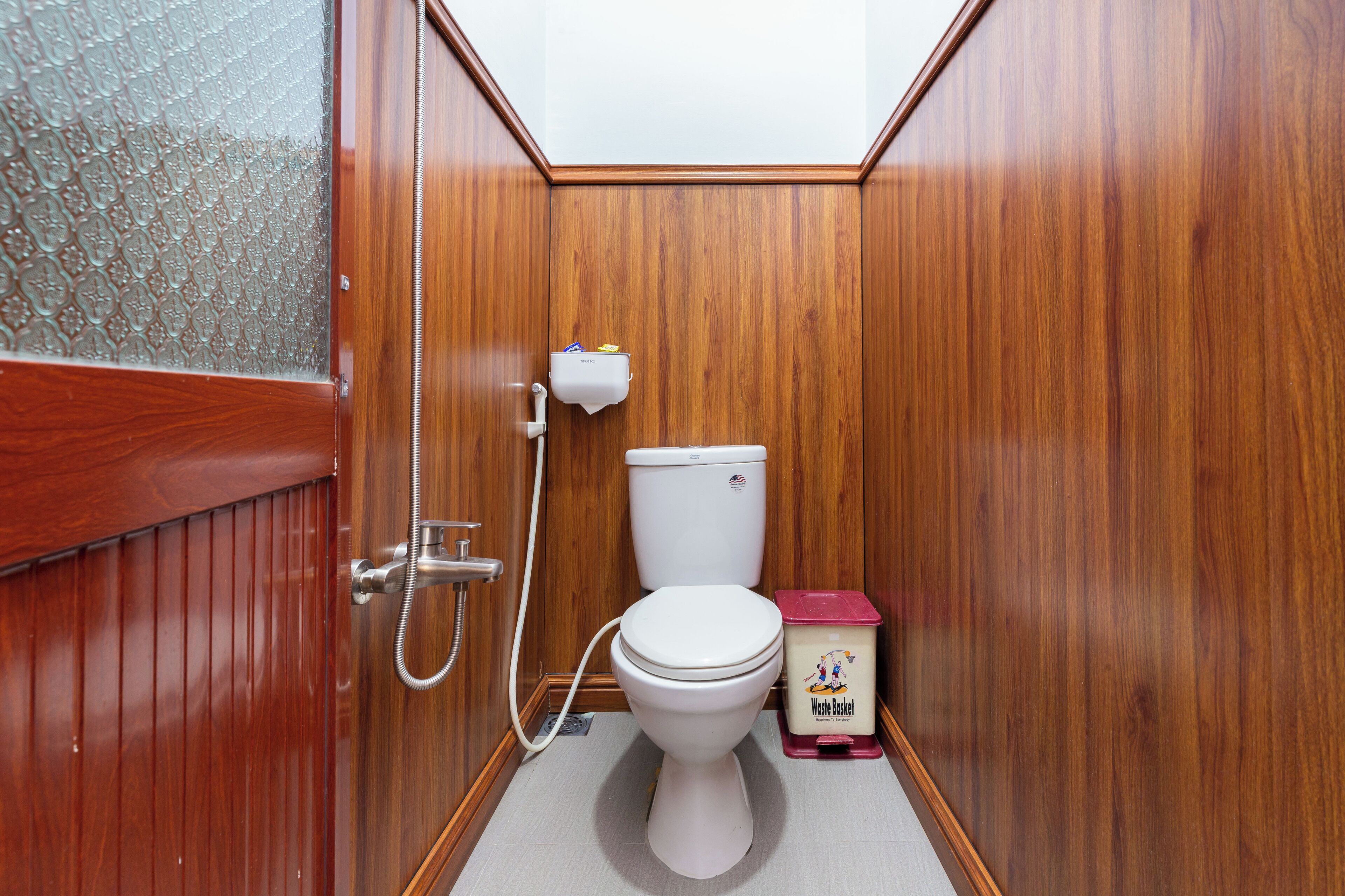Une petite salle de bain aux murs lambrissés, équipée de toilettes, d’un sèche-mains et d’une poubelle.