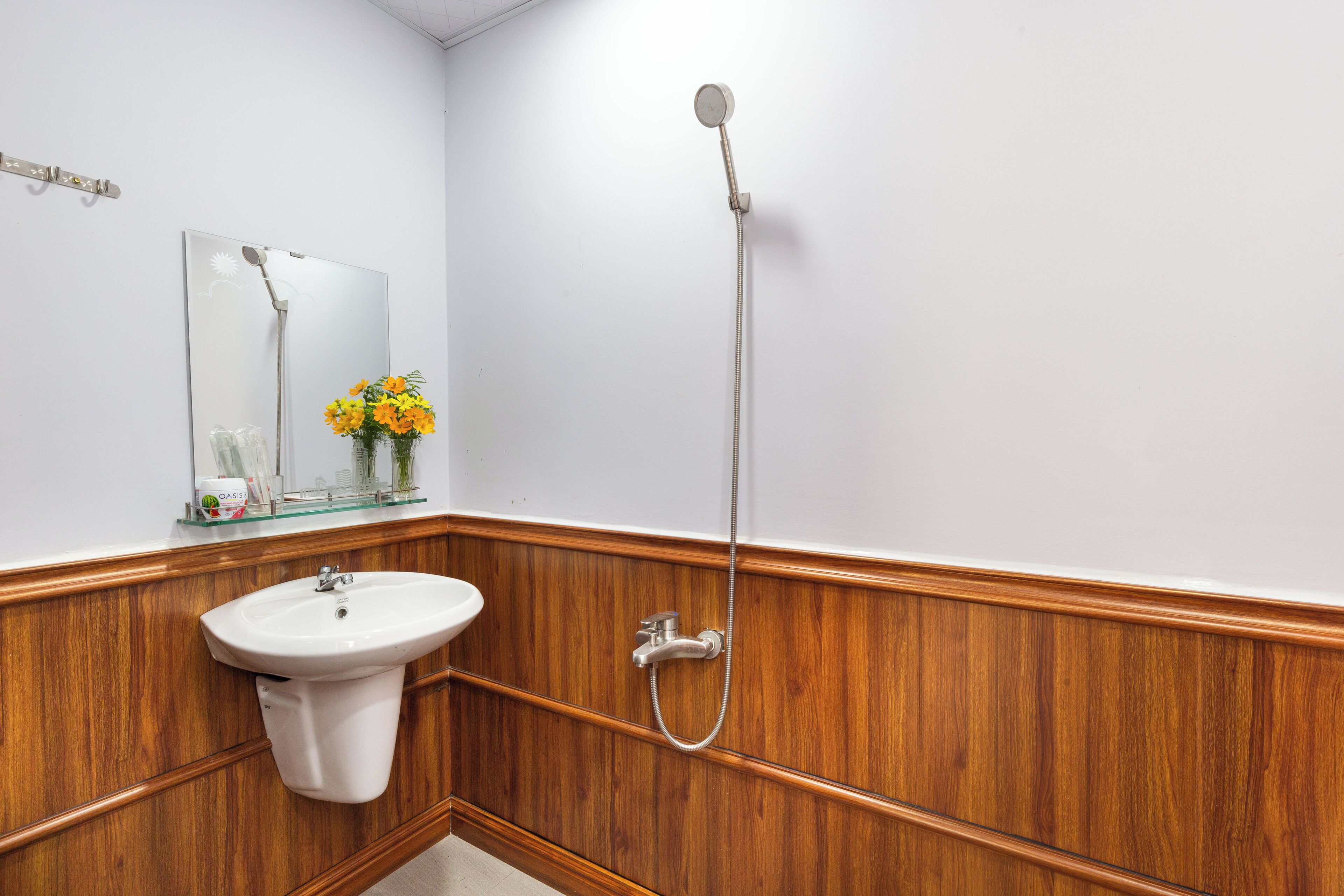 A bathroom with a wooden panel wall, a white sink, a mirror, and a shower.