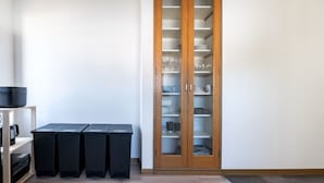 Una stanza con un mobile in legno dotato di vetrine che contengono piatti, bicchieri e tazze. Sulla parete sono presenti tre contenitori neri.