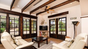 A living room with a TV, leather sofas, a coffee table, and large windows with a view of greenery. - Villa Estrella Del Mar- Hacienda Pinilla (Hacienda pinilla)