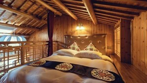Ein Zimmer in einer Holzhütte mit einem Bett, einer Wandlampe und Blick durch ein Holzgitterfenster.