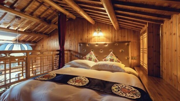 Une pièce de cabane en bois comprenant un lit, une applique murale décorative et une vue à travers une fenêtre à treillis de bois.