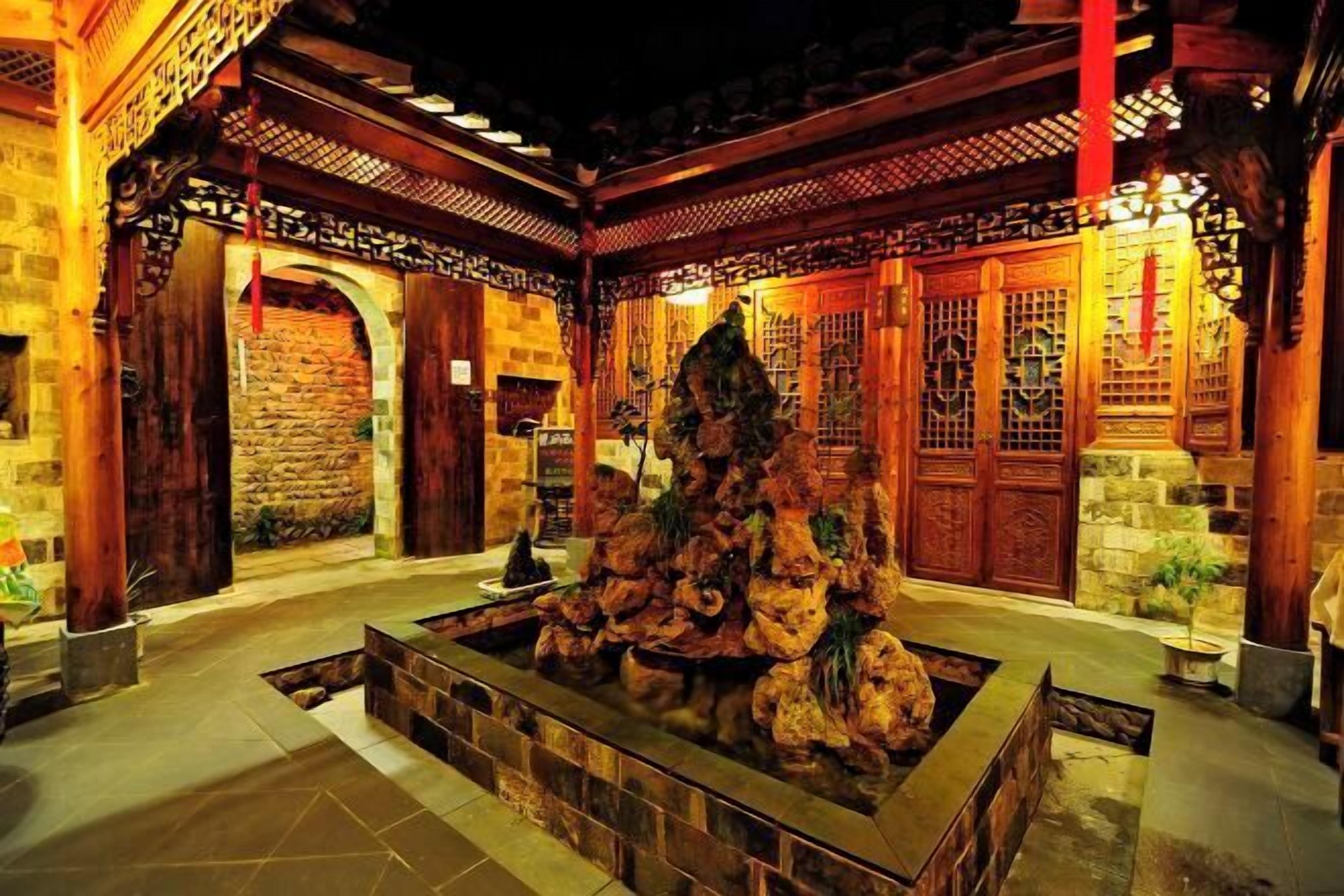 A traditional courtyard with stone walls, wooden gates, and a central rock formation.