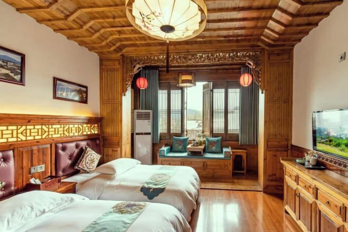 Une chambre de style traditionnel avec un plafond en bois, un lit doté d’une tête de lit, un coin salon avec des coussins et un téléviseur posé sur un meuble en bois.
