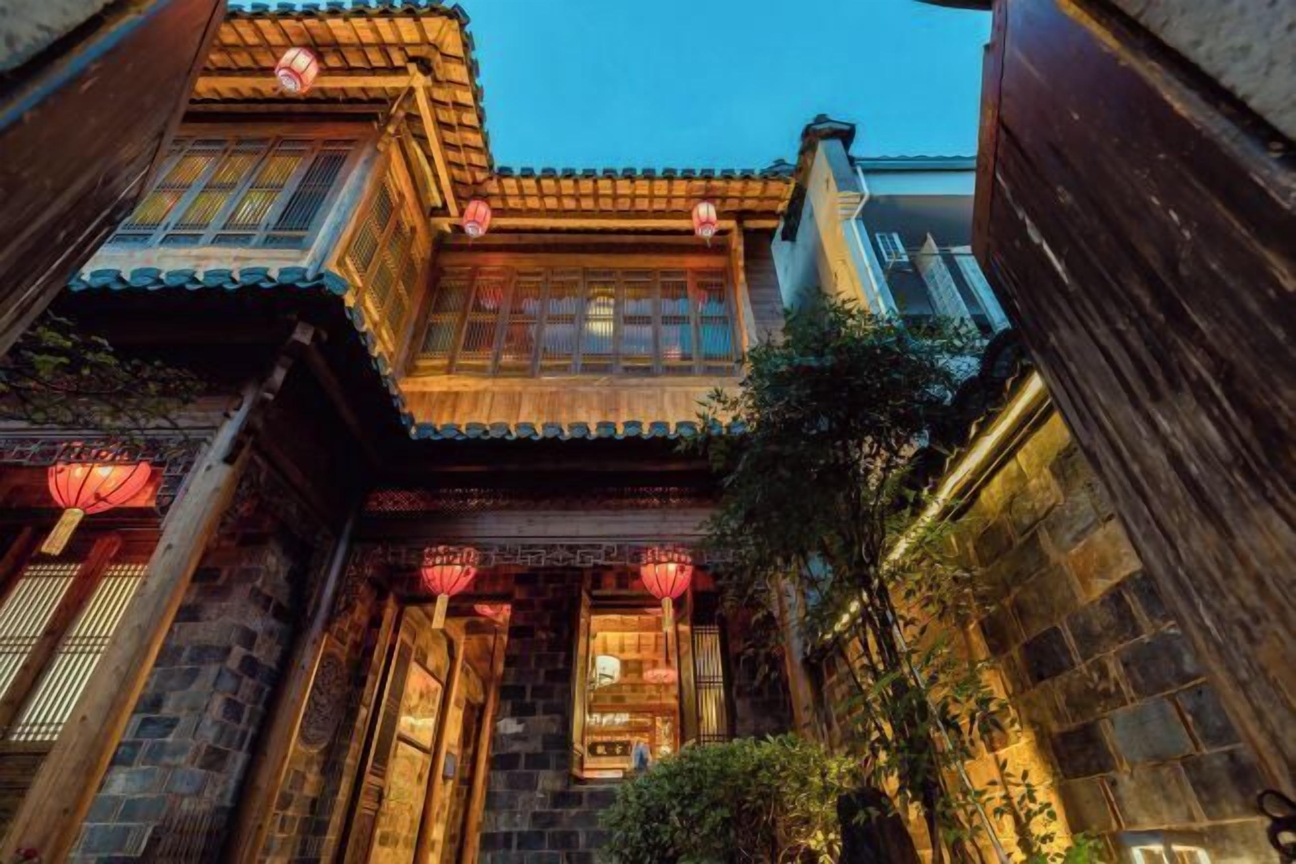 A traditional courtyard with wooden buildings, stone walls, and red lanterns.