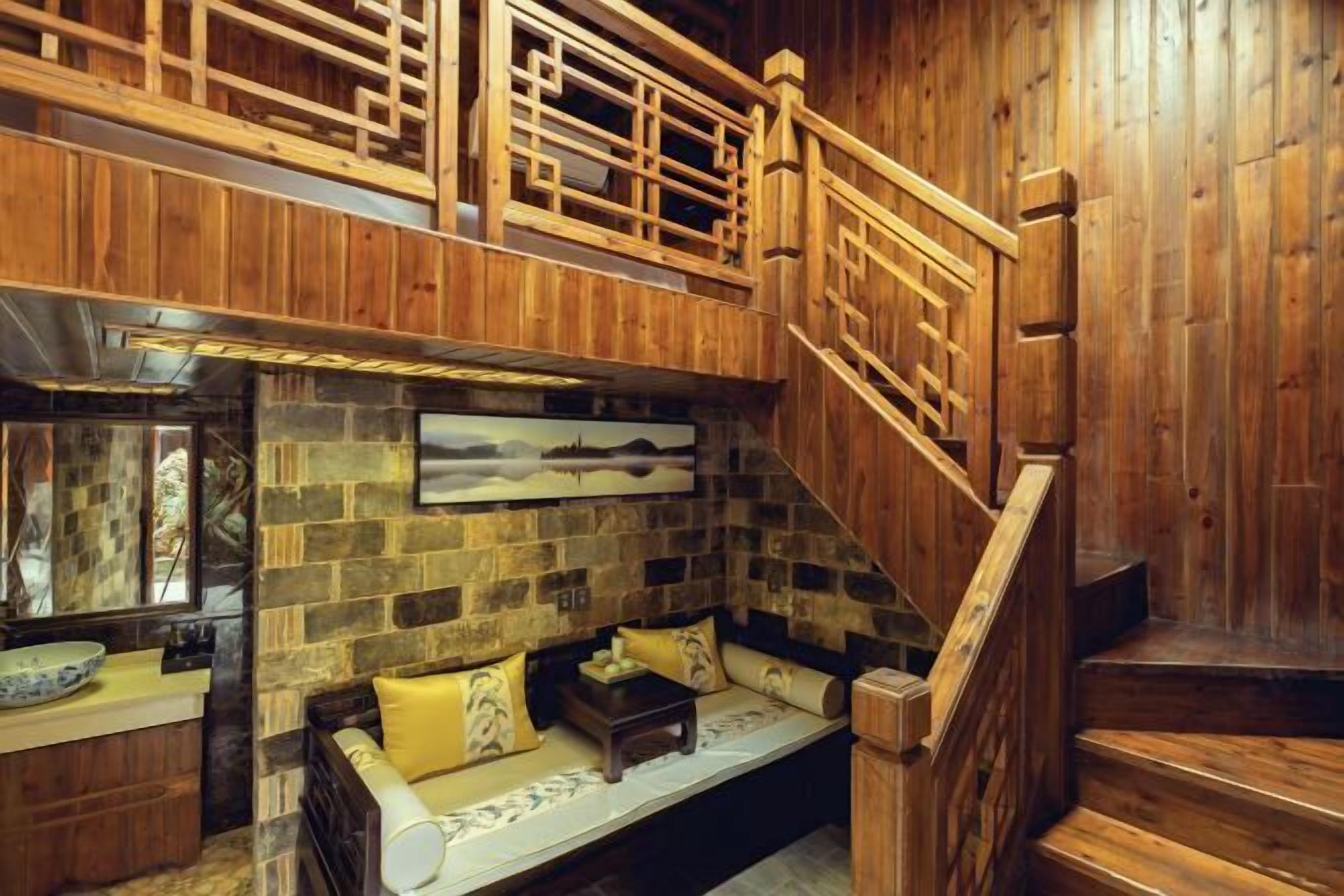 A wooden interior with a stone wall, a wooden staircase, and a seating area with cushions.
