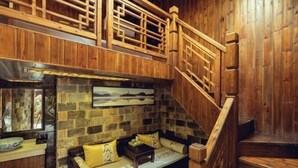 Un intérieur en bois avec un mur en pierre, un escalier en bois et un coin salon agrémenté de coussins.