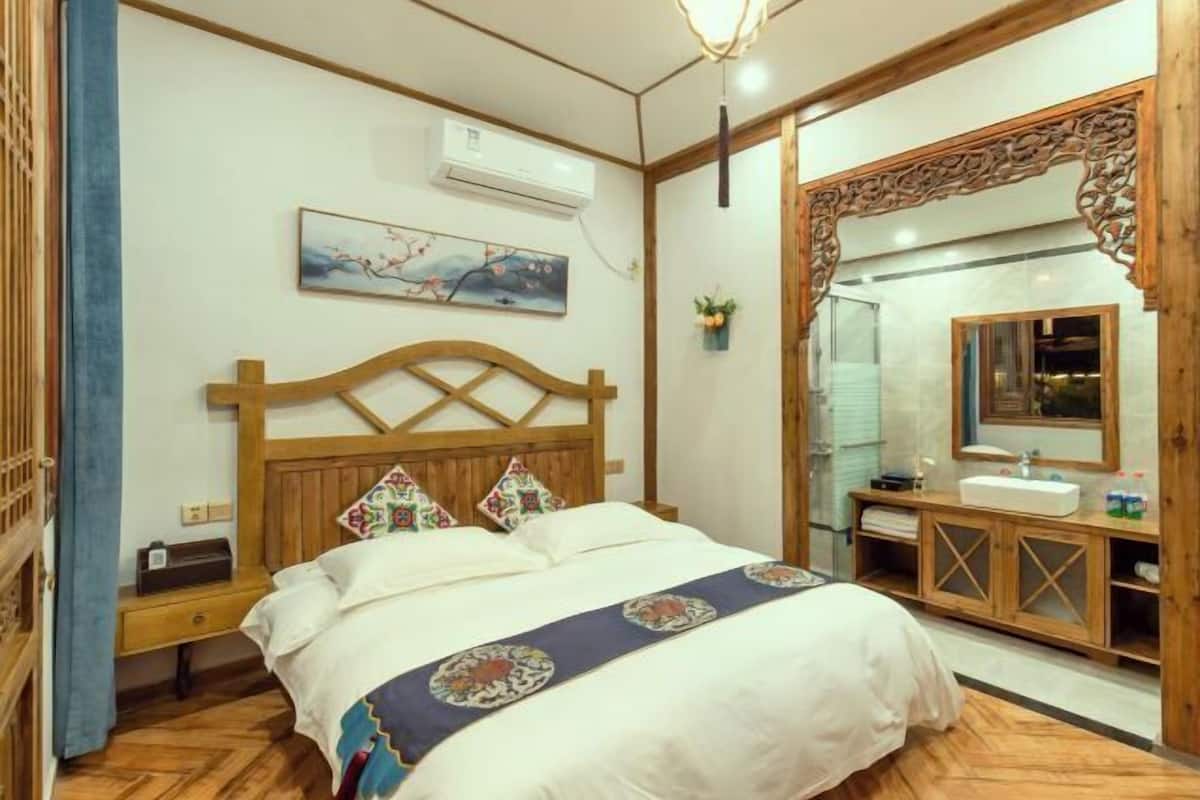 Une chambre à coucher avec un lit en bois, une table de chevet et un miroir, ainsi qu’une salle de bain équipée d’un lavabo et d’un miroir.