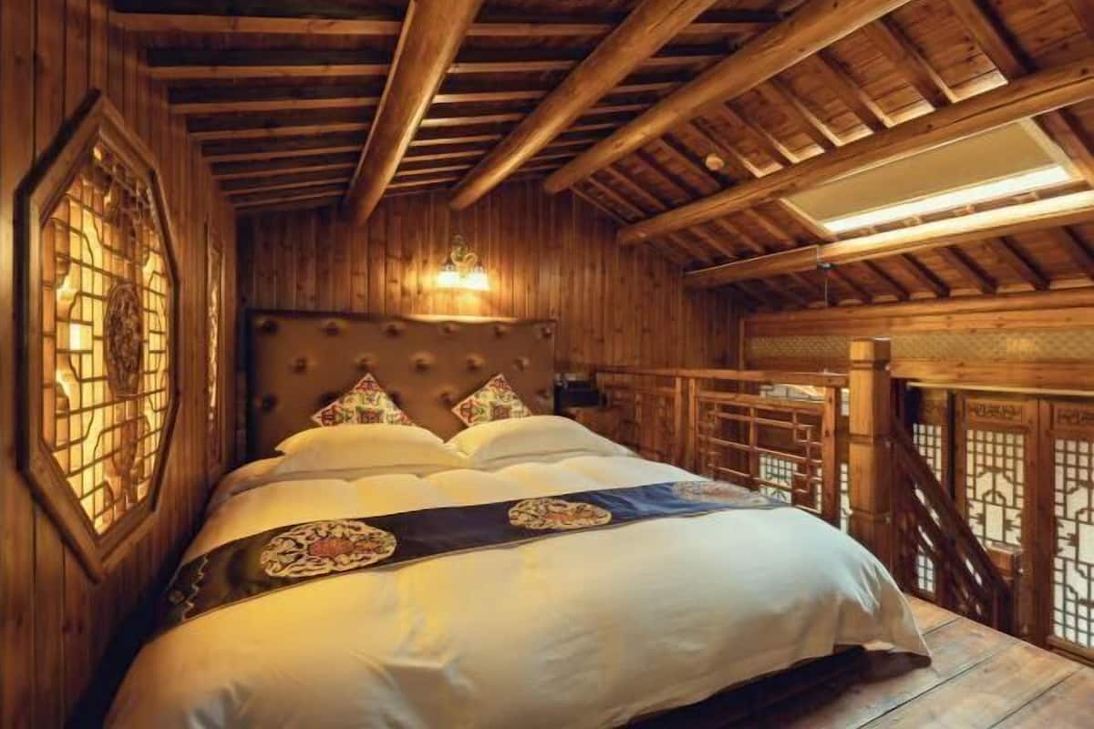 Un intérieur en bois comprenant un lit, une fenêtre ornée d’un motif décoratif et une structure de plafond en bois.