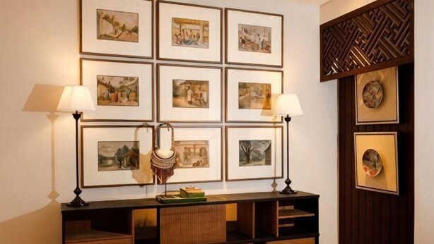 A room with a wall-mounted shelf displaying framed artwork, a sideboard with drawers, and two wall-mounted lamps.