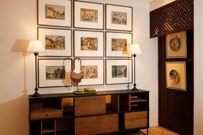 Een kamer met een wandplank waarop ingelijste kunstwerken staan, een dressoir met lades, en twee wandlampen.