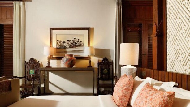 Quarto de hotel com uma cama, mesa de cabeceira com abajur, espelho e parede com padrão geométrico.