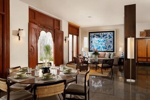 A dining area with a round table set for four, flanked by wicker chairs, a large abstract painting on the wall, and a modern floor lamp. - The Tulou Bali by Nakula (Bali)