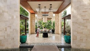A lobby with a wooden floor, a central seating area, and a view of greenery outside.