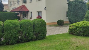 A two-story building with a red-tiled roof, a satellite dish, and a small garden area with trimmed bushes and a paved walkway. - Hotel and guesthouse good value for money (Hochkirch)