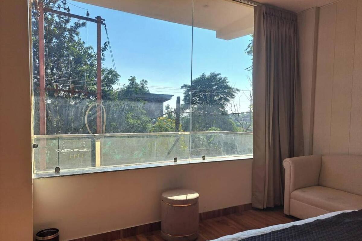 Habitació d'hotel amb una finestra gran, un llit, un tamboret petit rodó i un sofà beix.
