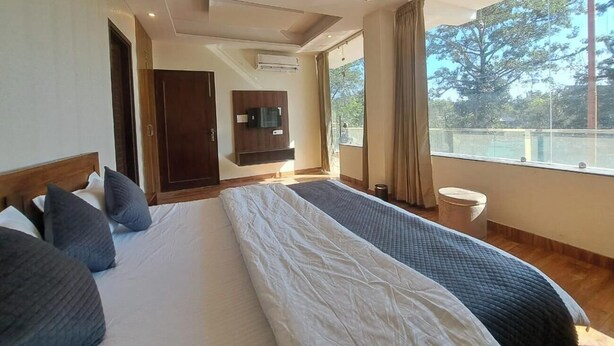 A hotel room with a large bed, a TV, and a balcony with a view of trees. - Castle Inn Homestay  (Dehradun)