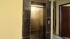 A hallway with a marble-tiled floor and a door leading to an elevator. - Castle Inn Homestay  (Dehradun)