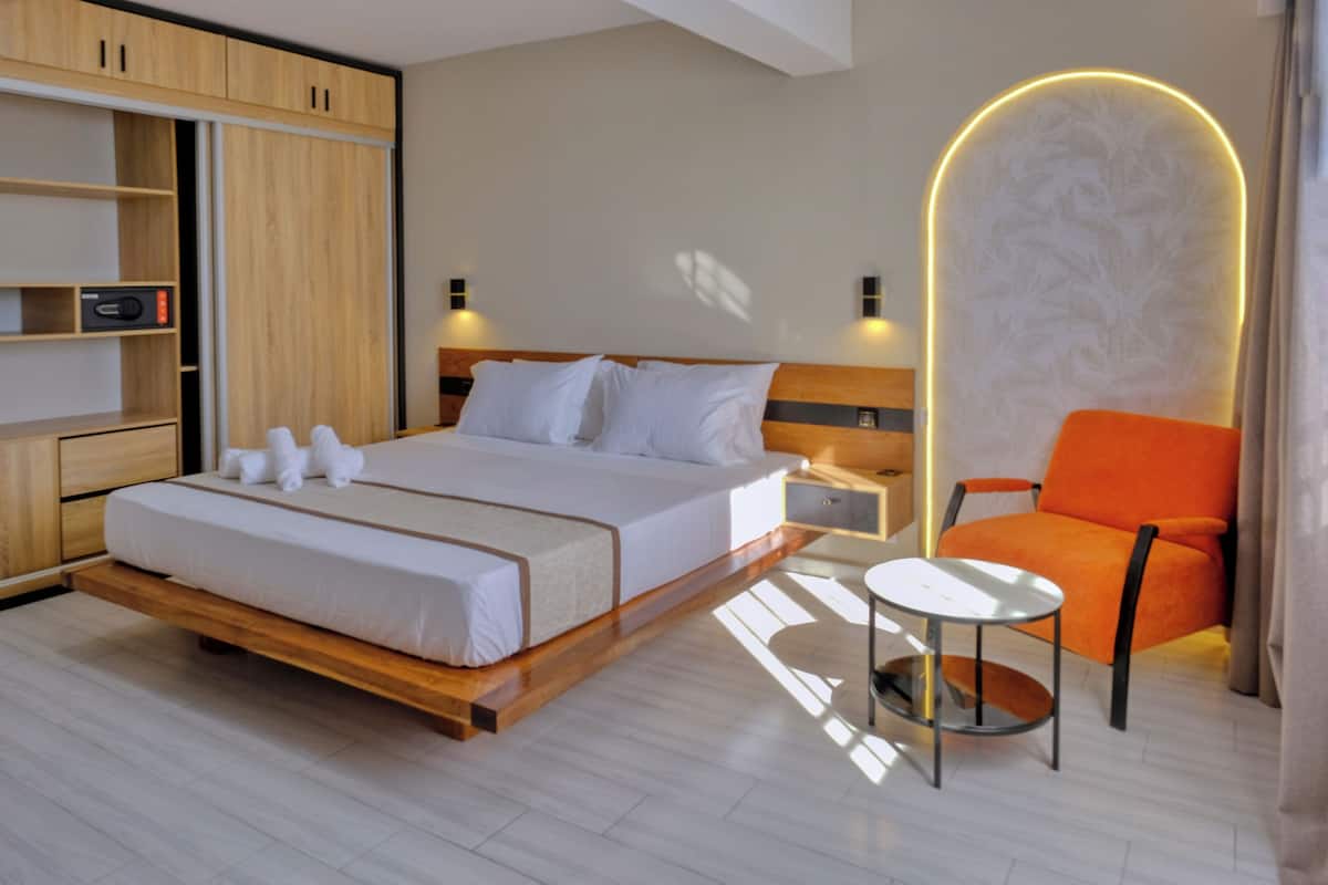 Una habitación de hotel moderna con una cama grande, un armario de madera, una mesita de noche y una silla naranja.