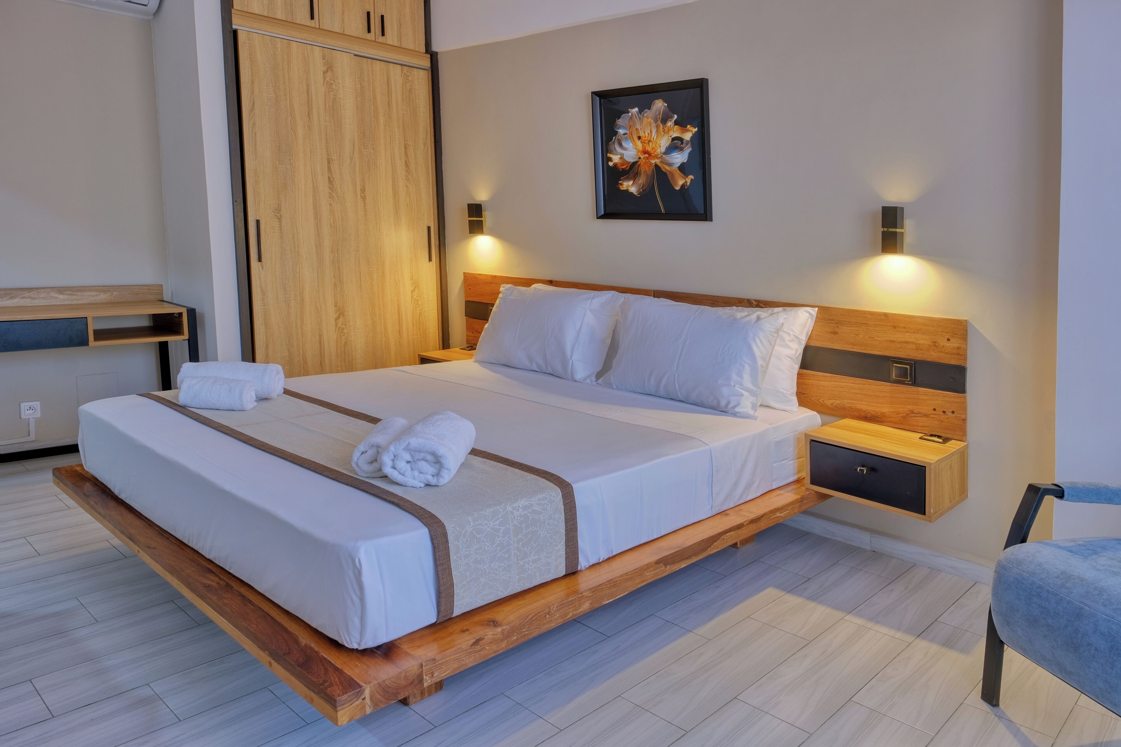 Une chambre moderne avec un cadre de lit en bois, du linge de lit blanc, une table de chevet, une étagère murale et un tableau.