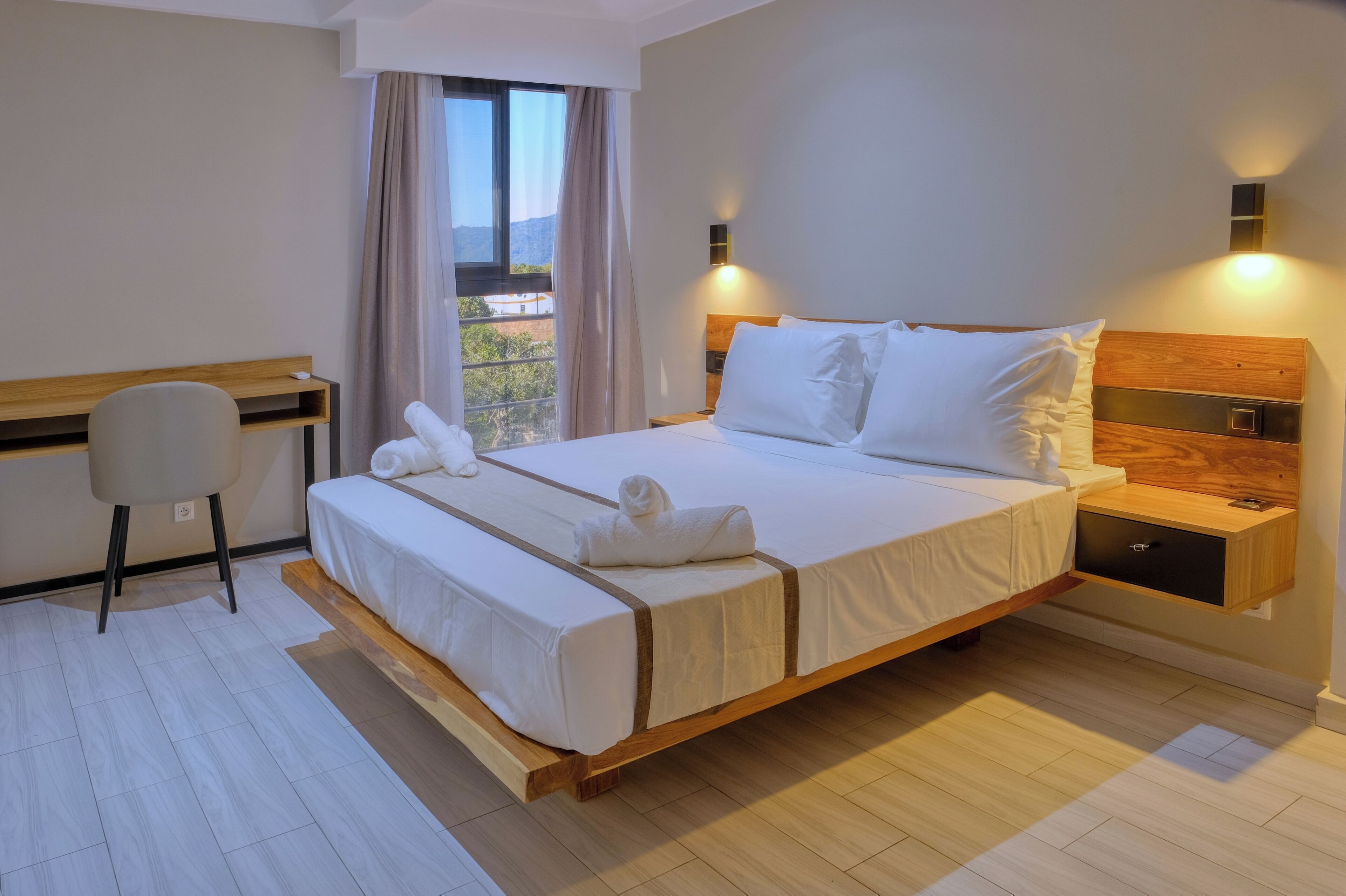 A modern hotel room with a large bed, a desk, and a view of the outdoors.