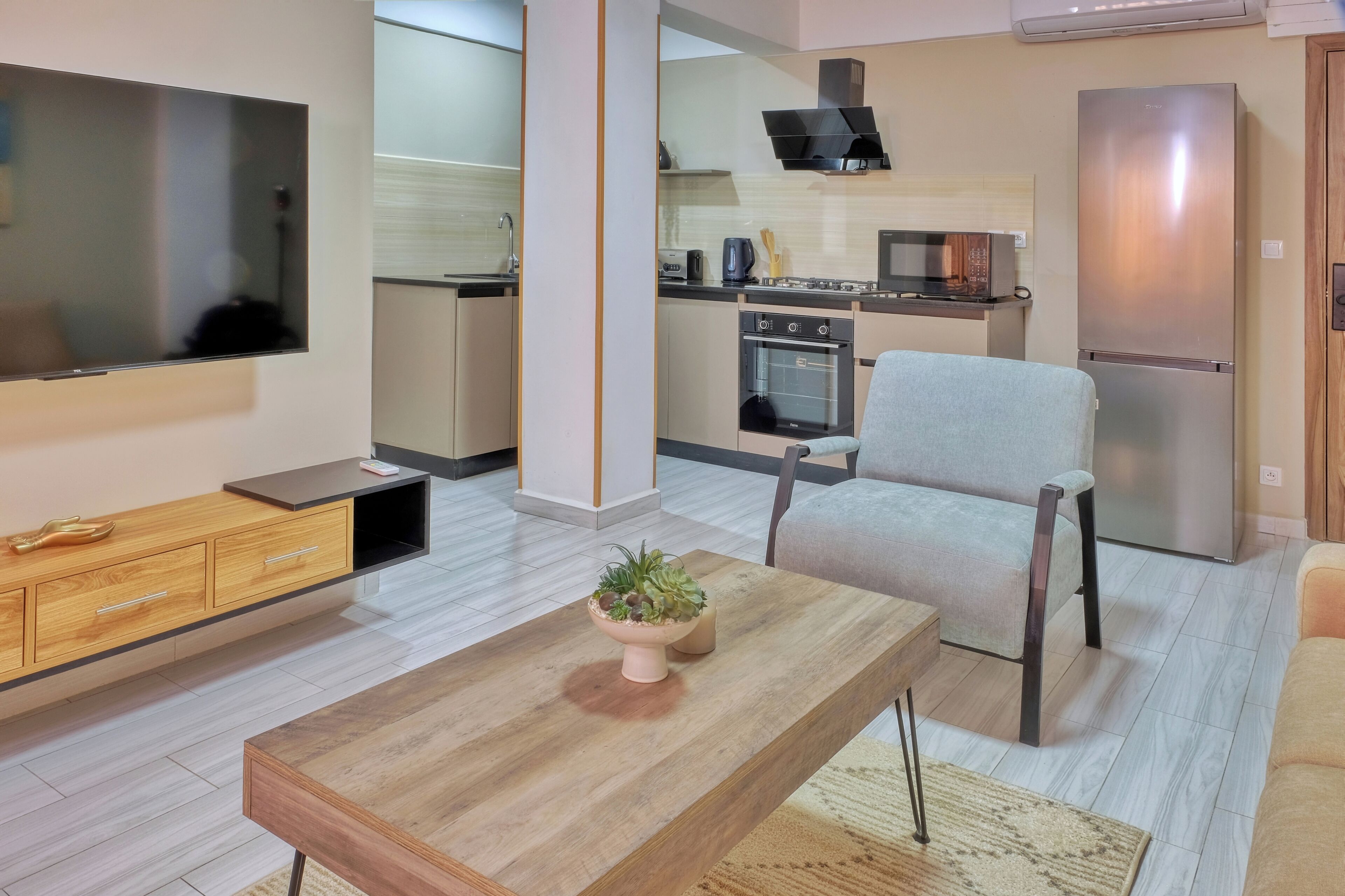 A modern living room with a flat-screen TV, wooden coffee table, and a grey armchair.