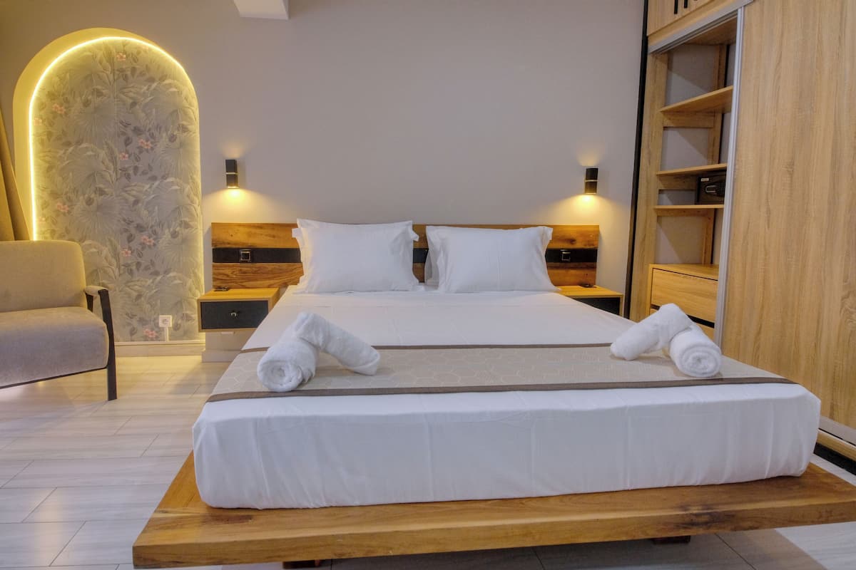 Una habitación de hotel moderna con una cama grande, dos mesitas de noche, un cabecero de madera, un armario de madera y una silla.