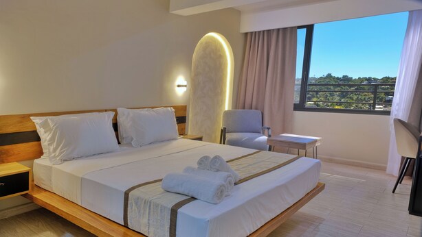 A modern hotel room with a large bed, bedside tables, a chair, and a view of the outdoors. - ZEN Hôtel (Nosy Be)