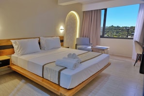 A modern hotel room with a large bed, bedside tables, a chair, and a view of the outdoors. - ZEN Hôtel (Nosy Be)
