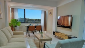 A modern living room with a sofa, dining table, chairs, a TV, and a large window with a view. - ZEN Hôtel (Nosy Be)