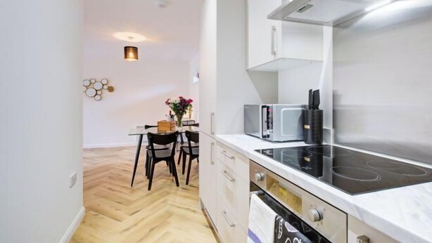 Une cuisine compacte dotée d’une cuisinière moderne, d’un four à micro-ondes et de meubles de rangement blancs.