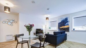 Un salon moderne avec une table à manger en verre, deux chaises, un canapé bleu et un téléviseur à écran plat.