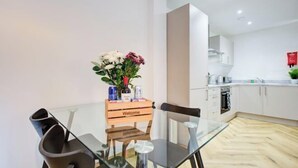 Une cuisine moderne avec des meubles blancs, une pancarte d’accueil en bois et une table en verre avec des chaises.